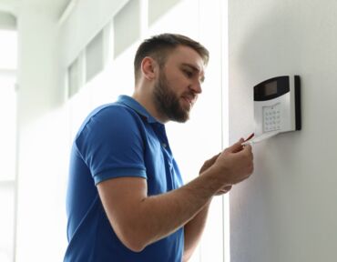Mann installiert Haussicherheitssystem an weißer Wand im Zimmer