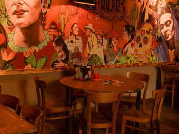 Das Restaurant Sausalitos von innen. Mehrere Holztische mit Stühlen im Vordergrund. Eine bunt bemalte Wand mit kreativen Kunstgesichtern im Fokus.