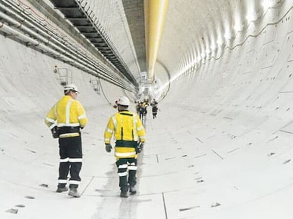 Zwei Monteure mit gelber Sicherheitskleidung und weißem Helm gehen im inneren eines weißen Tunnels.